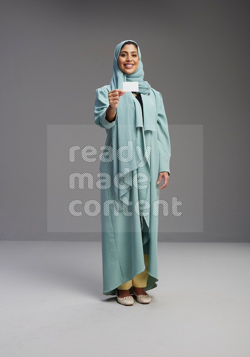 Saudi Woman wearing Abaya standing holding ATM card on Gray background