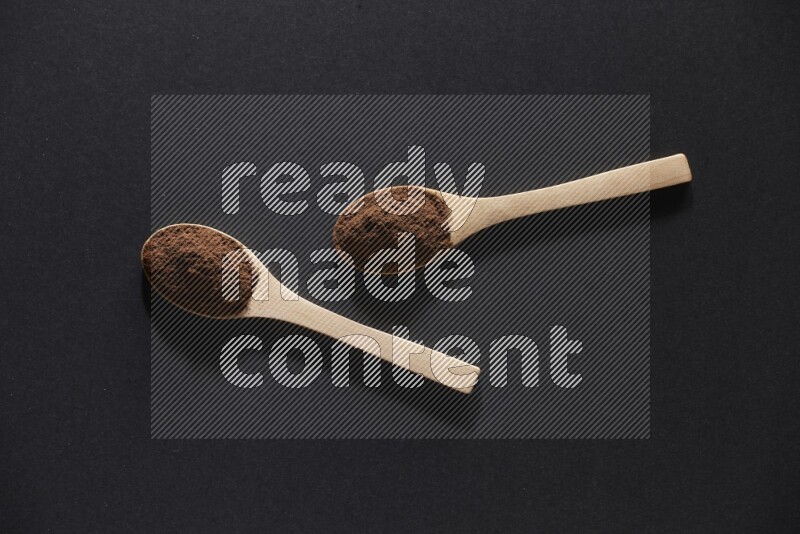 2 wooden spoons full of cloves powder on a black flooring