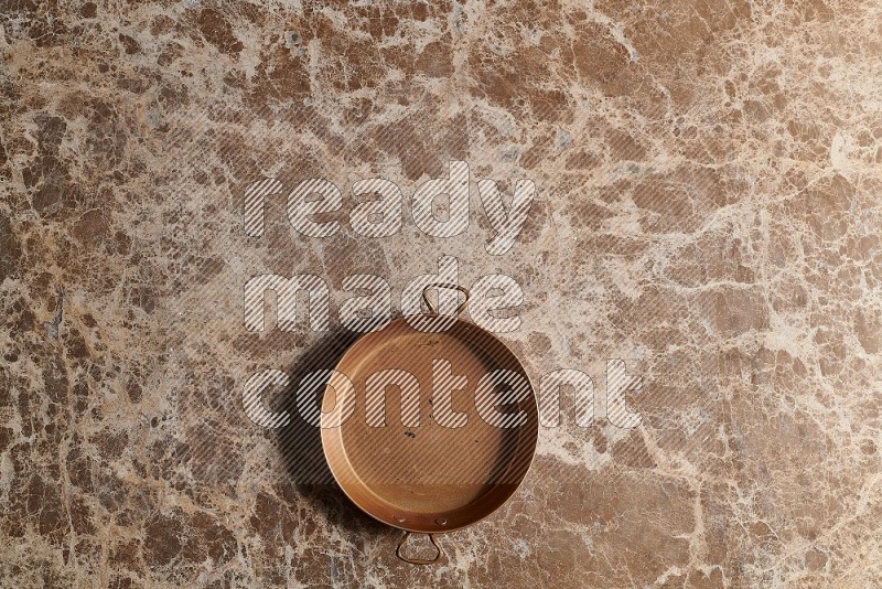 Top View Shot Of A Small Copper pan On beige Marble Flooring