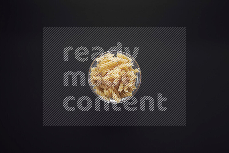 Fusilli pasta in a glass bowl on black background