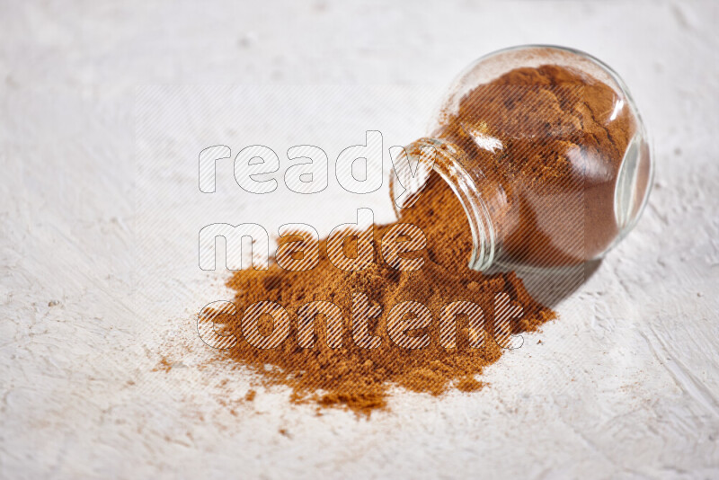 A glass jar full of ground paprika powder flipped with some spilling powder on white background