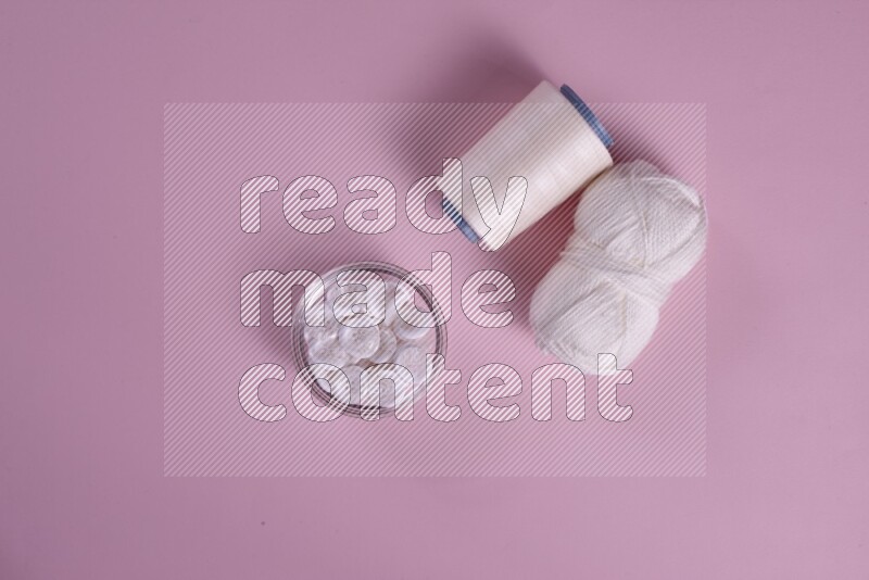 A white and pink collection of sewing and tailoring tools arranged on a pink background