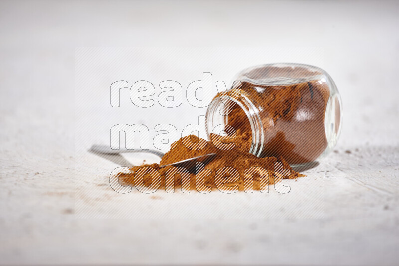 A glass jar full of ground paprika powder flipped with some spilling powder on white background