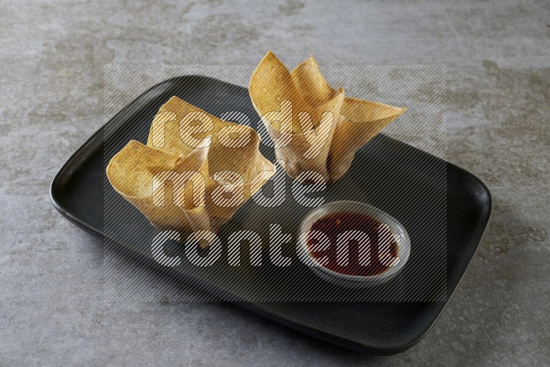 wonton cups with soy sauce ramkin on rectangle dark grey ceramic plate on grey textured counter top