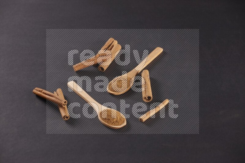 Two wooden spoons full of cinnamon powder with cinnamon sticks on black background