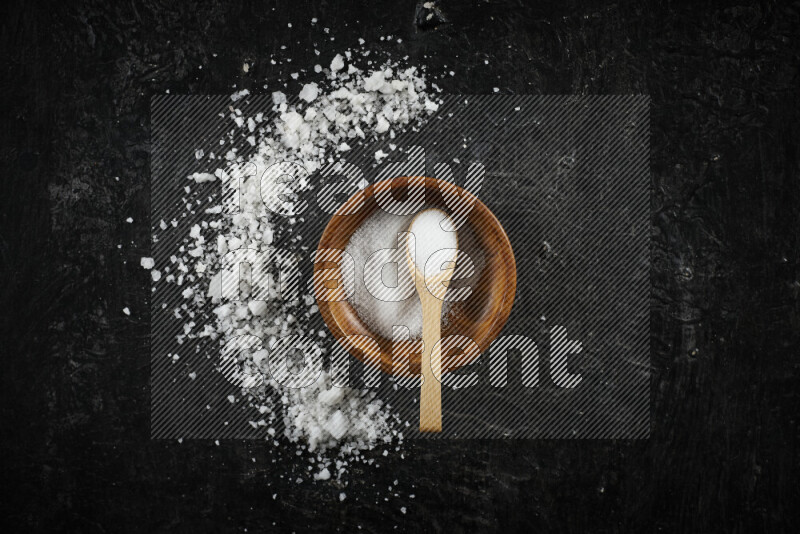 A pottery plate full of fine salt with bunch of coarse salt beside it on black background