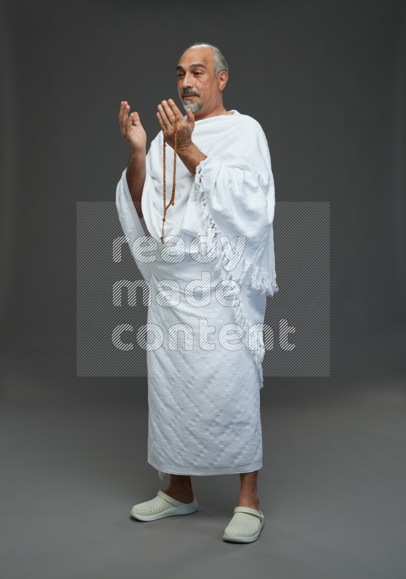 A man wearing Ehram Standing dua'a on gray background