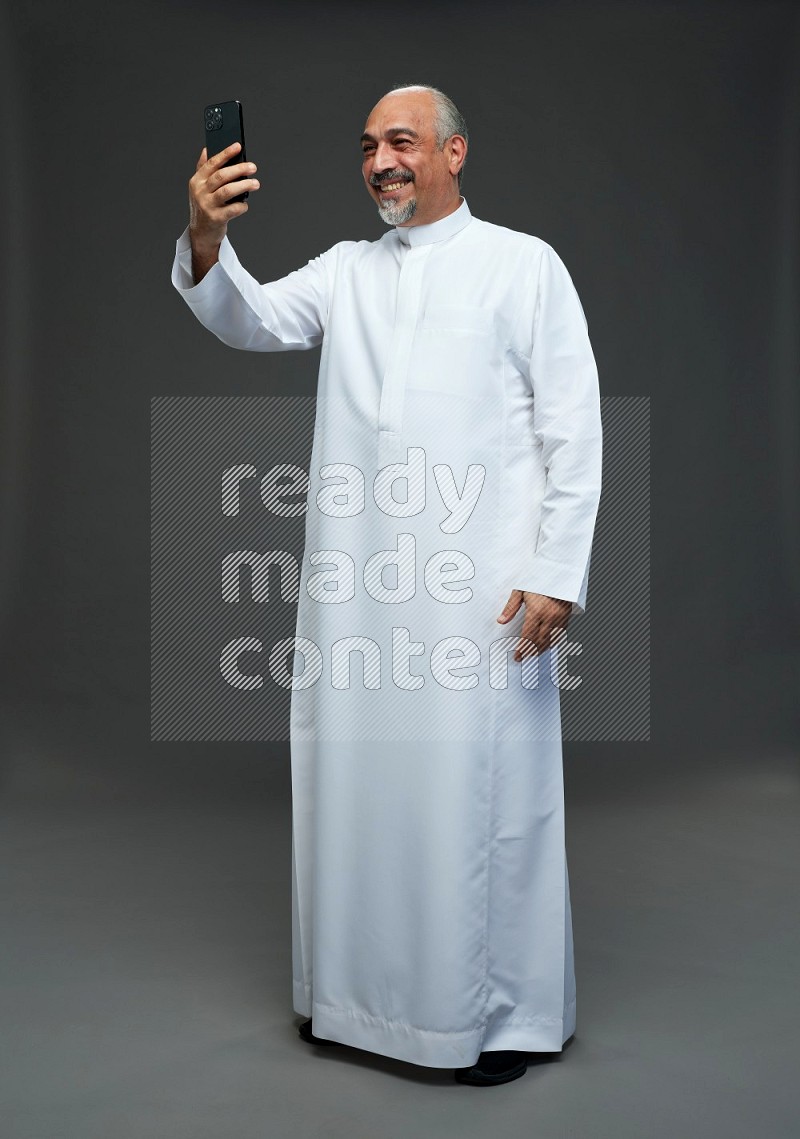 Saudi man without shomag Standing taking selfie on gray background