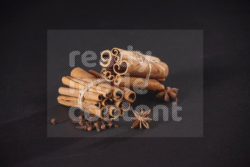 Two bounded stacks of cinnamon sticks with cloves and star anise on black background
