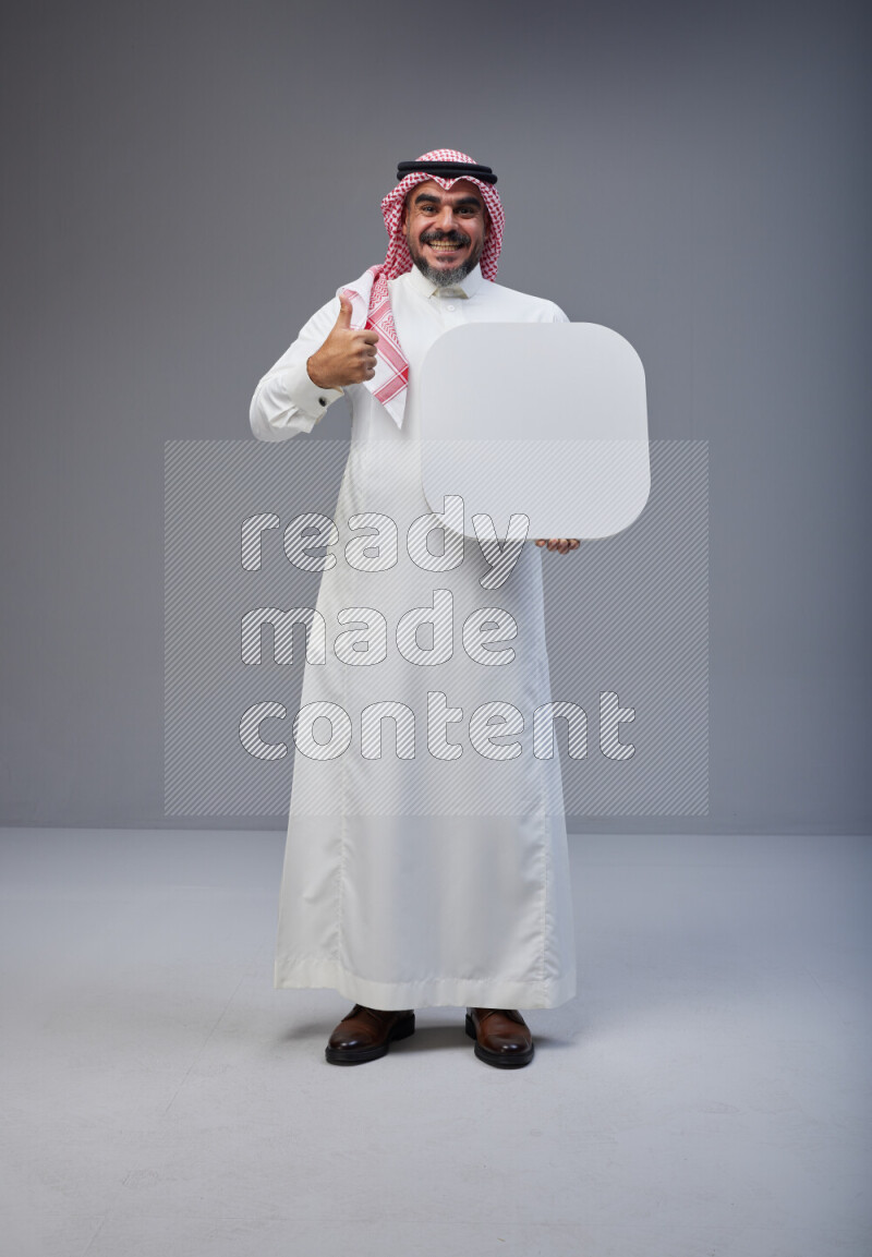 Saudi man Wearing Thob and red Shomag standing holding social media sign on Gray background