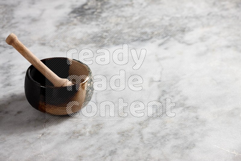 Multicolored Pottery bowl with wooden honey handle in it, on grey marble flooring, 45 degree angle