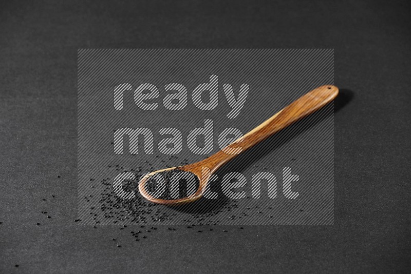 A wooden ladle full of black seeds and the seeds spread beside it on a black flooring