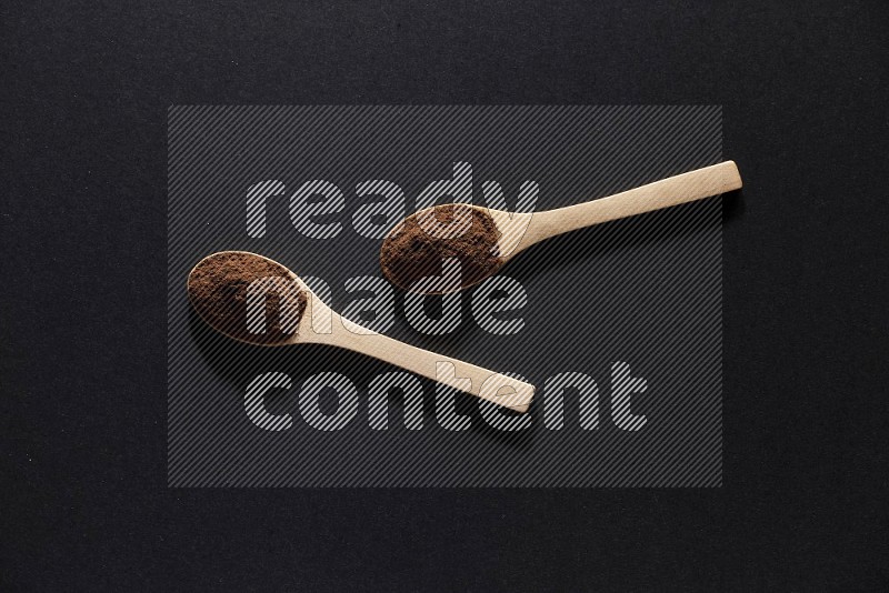 2 wooden spoons full of cloves powder on a black flooring