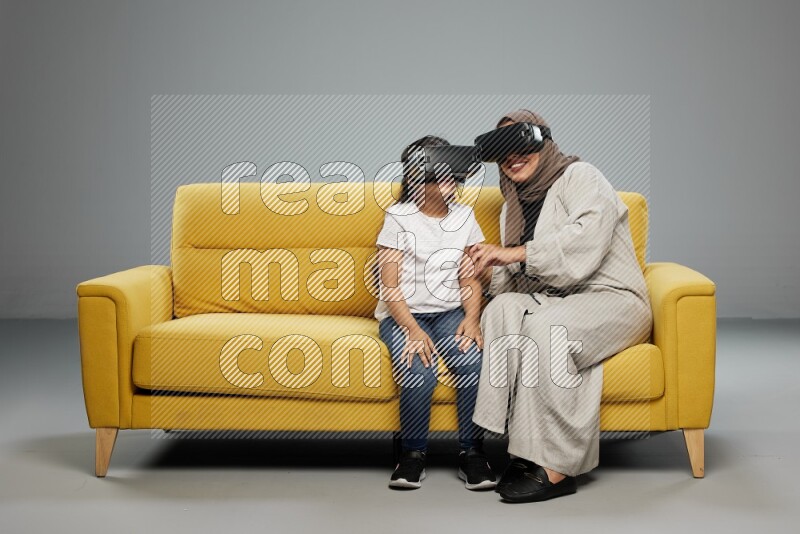 A girl and her mother sitting playing with VR on gray background