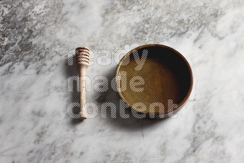 Multicolored Pottery Oven Plate with wooden honey handle on the side with grey marble flooring, 65 degree angle