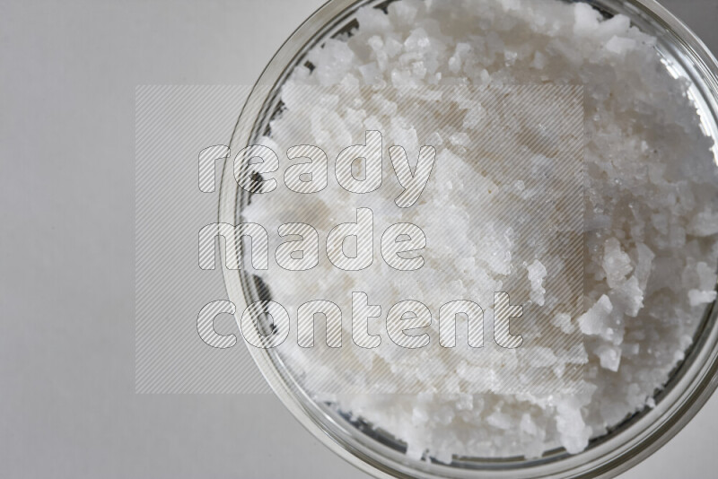 A glass bowl full of coarse sea salt crystals on white background