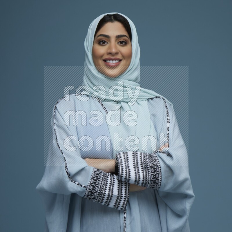 A woman posing in a blue background wearing a blue Abaya with hijab