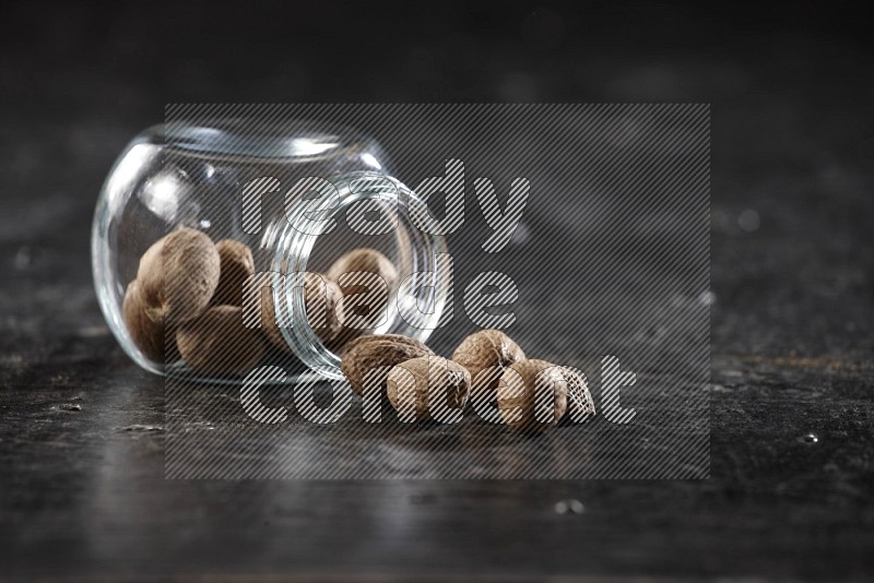 A glass spice jar full of nutmeg flipped and the seeds came out on a textured black flooring in different angles