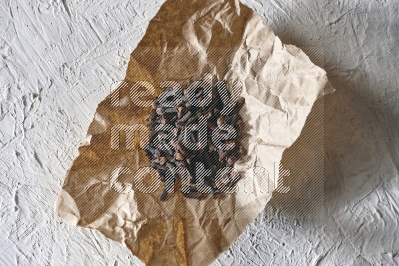 Cloves on crumpled piece of paper on a textured white flooring