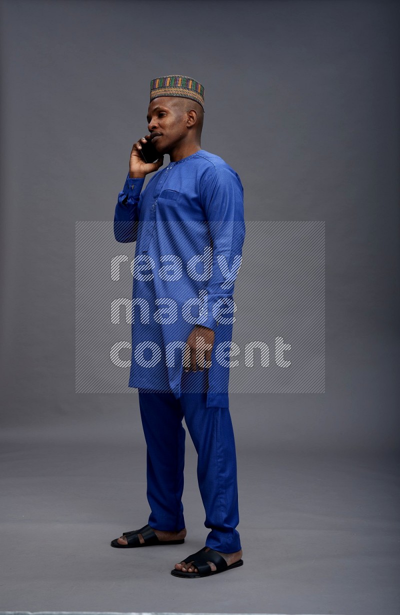 Man wearing Nigerian outfit standing talking on phone on gray background