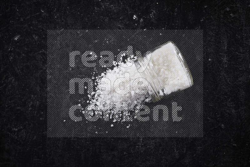 A glass jar full of coarse sea salt crystals on black background