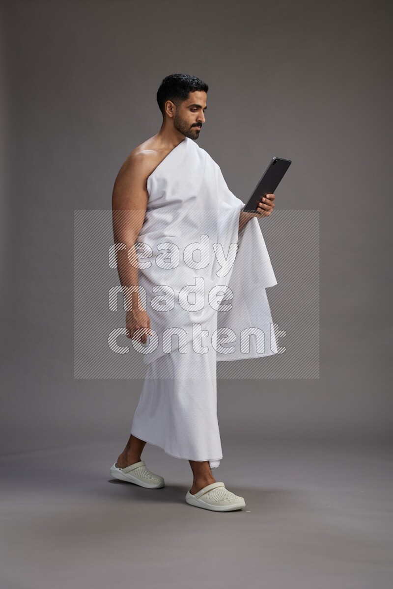 A man wearing Ehram and holding a tablet on gray background