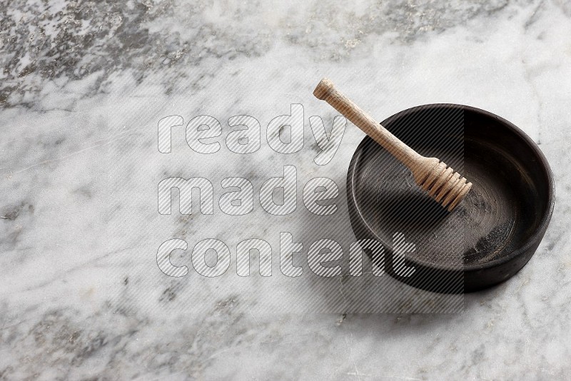 Black Pottery Oven Plate with wooden honey handle in it, on grey marble flooring, 65 degree angle