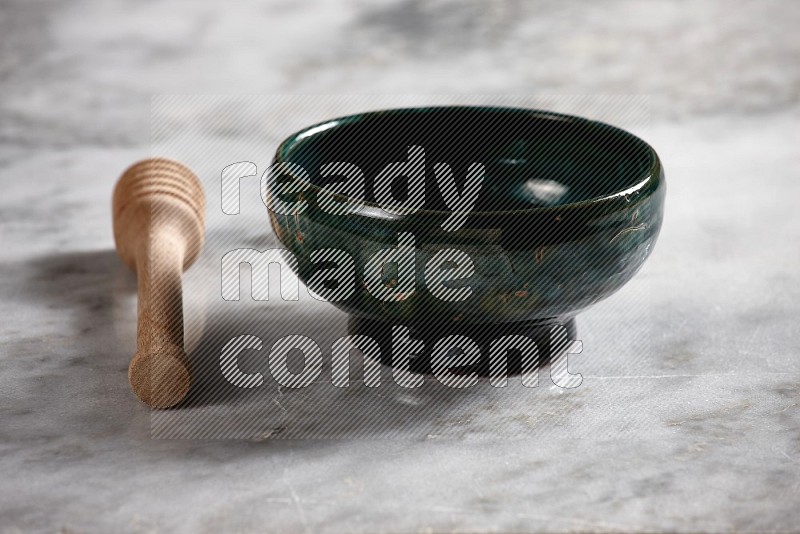 Dark Green Pottery bowl with wooden honey handle on the side with grey marble flooring, 15 degree angle