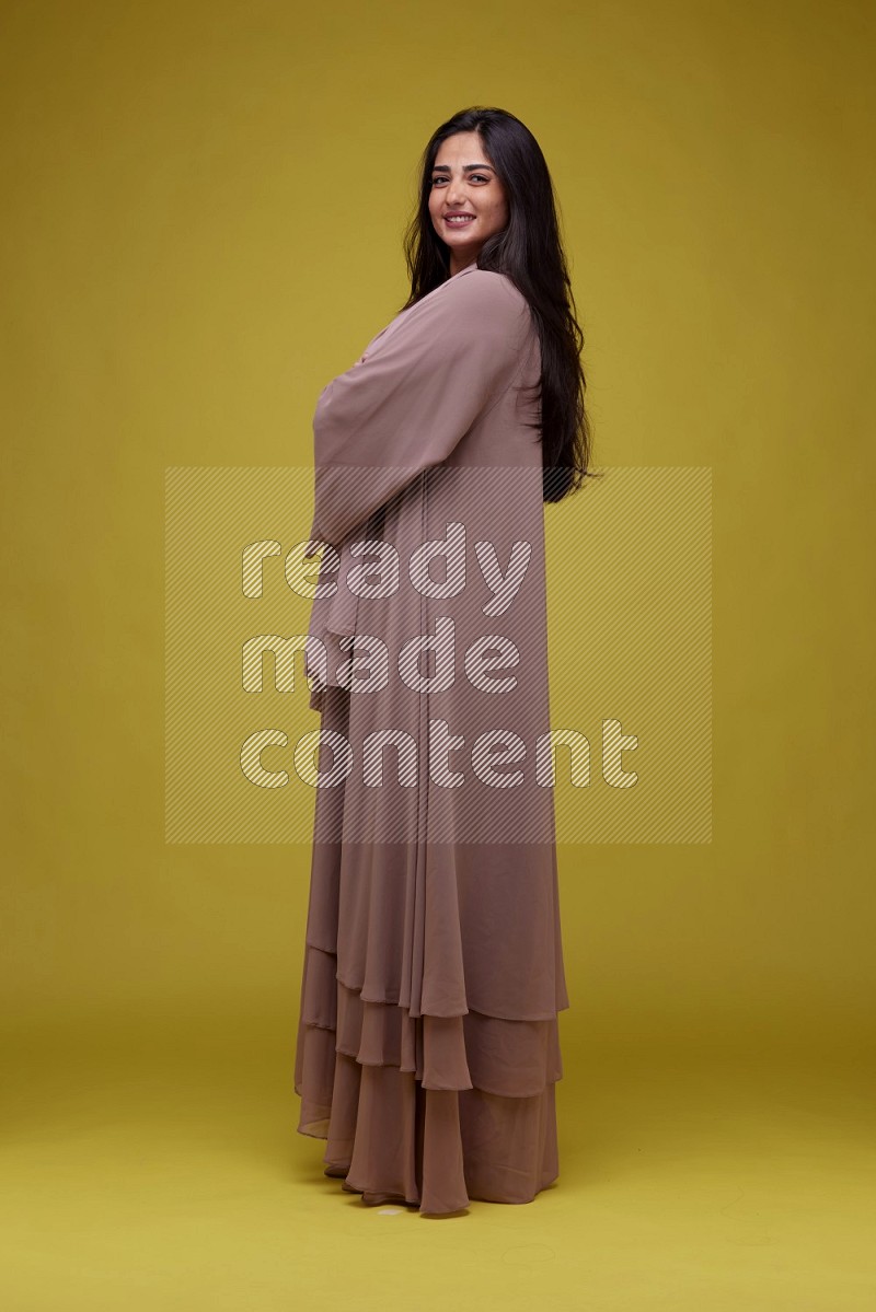 A woman Posing on a Yellow Background wearing Brown Abaya