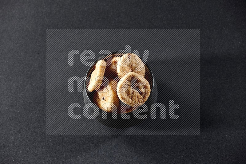 A black ceramic bowl full of dried figs on a black background in different angles
