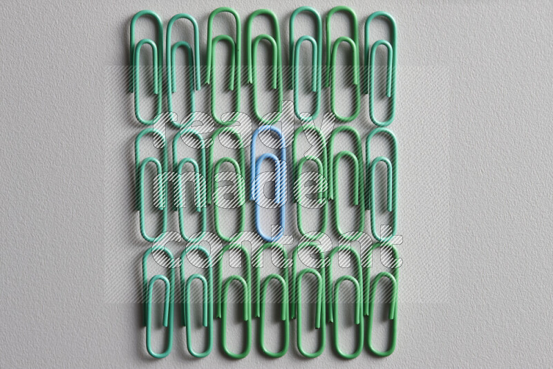 مجموعة من مشابك الورق الخضراء مع مشبك ورق ملون مختلف في المنتصف على خلفية رمادية