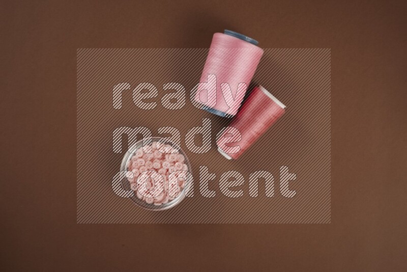 مجموعة من أدوات الخياطة والتفصيل زهرية اللون على خلفية بنية