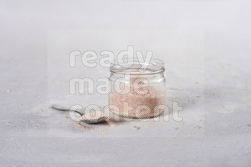 A glass jar full of fine himalayan salt on white background