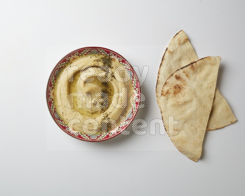 Hummus in a red plate with patterns garnished with zaatar & sumak on a white background