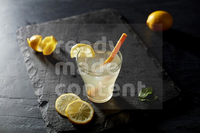 A glass of lemon juice with a straw on black background