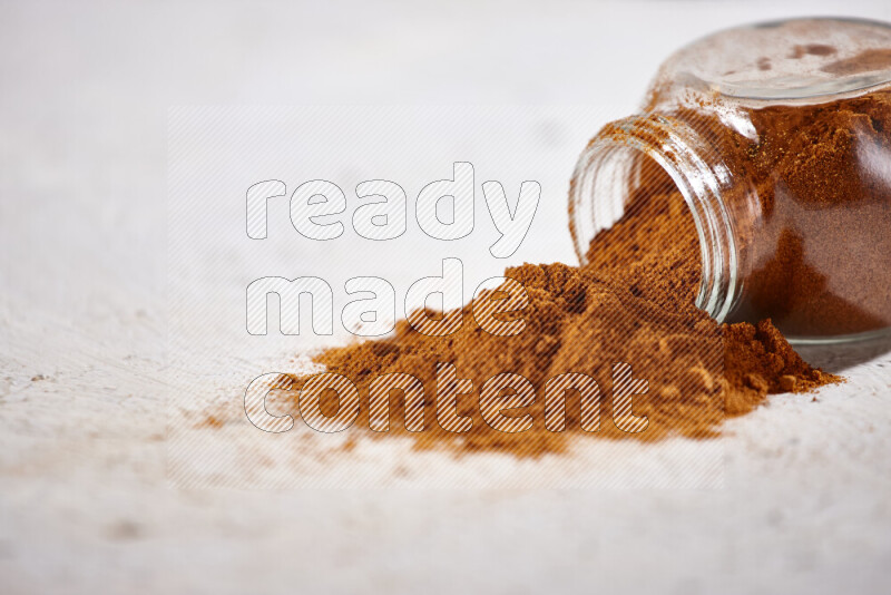 A glass jar full of ground paprika powder flipped with some spilling powder on white background