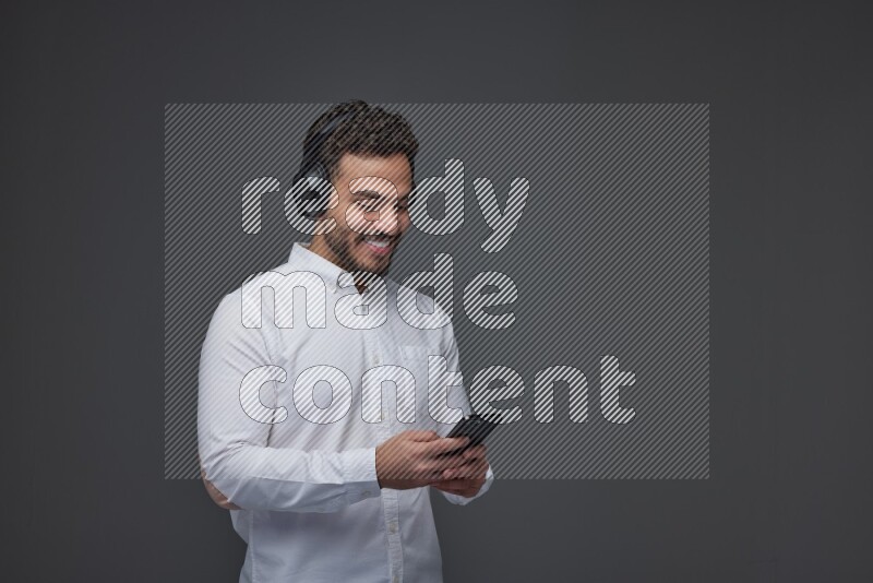 A man wearing smart casual and using his phone and headphone eye level on a gray background
