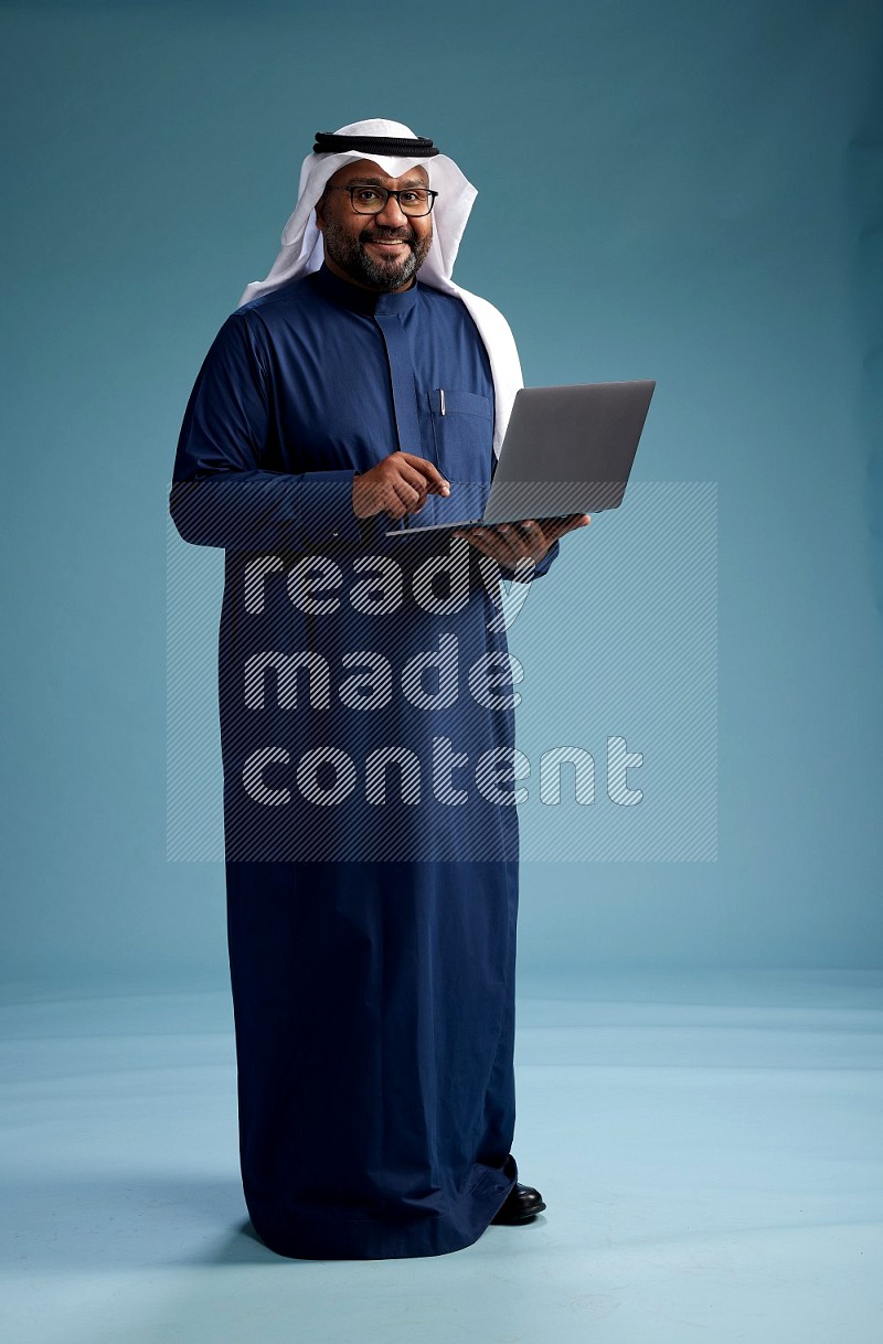 Saudi Man with shimag Standing working on laptop on blue background
