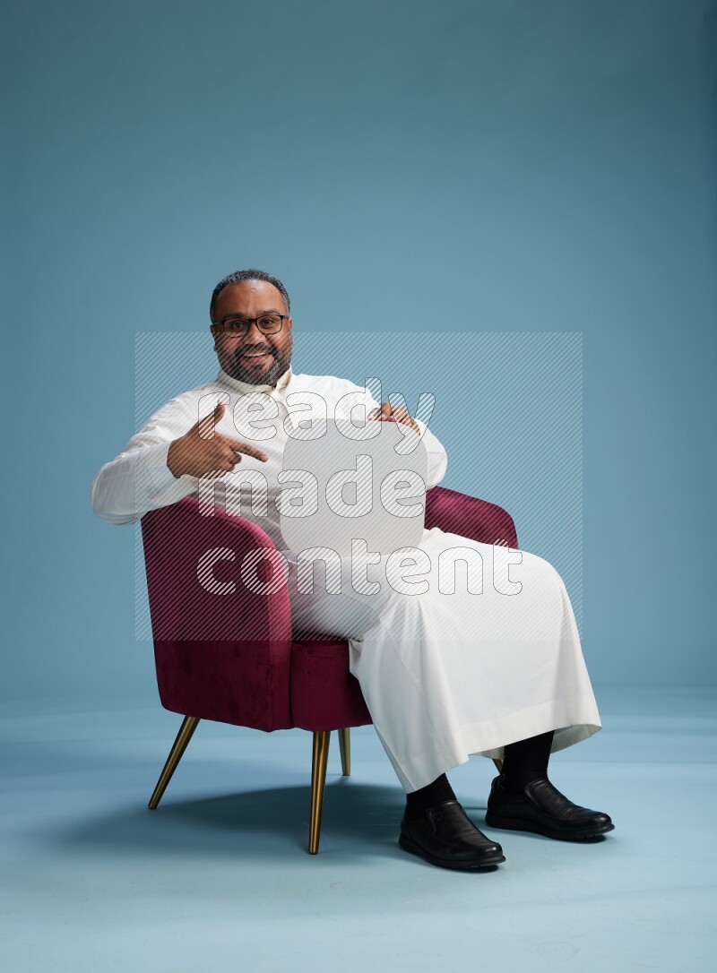 Saudi Man without shimag sitting on chair holding social media sign on blue background