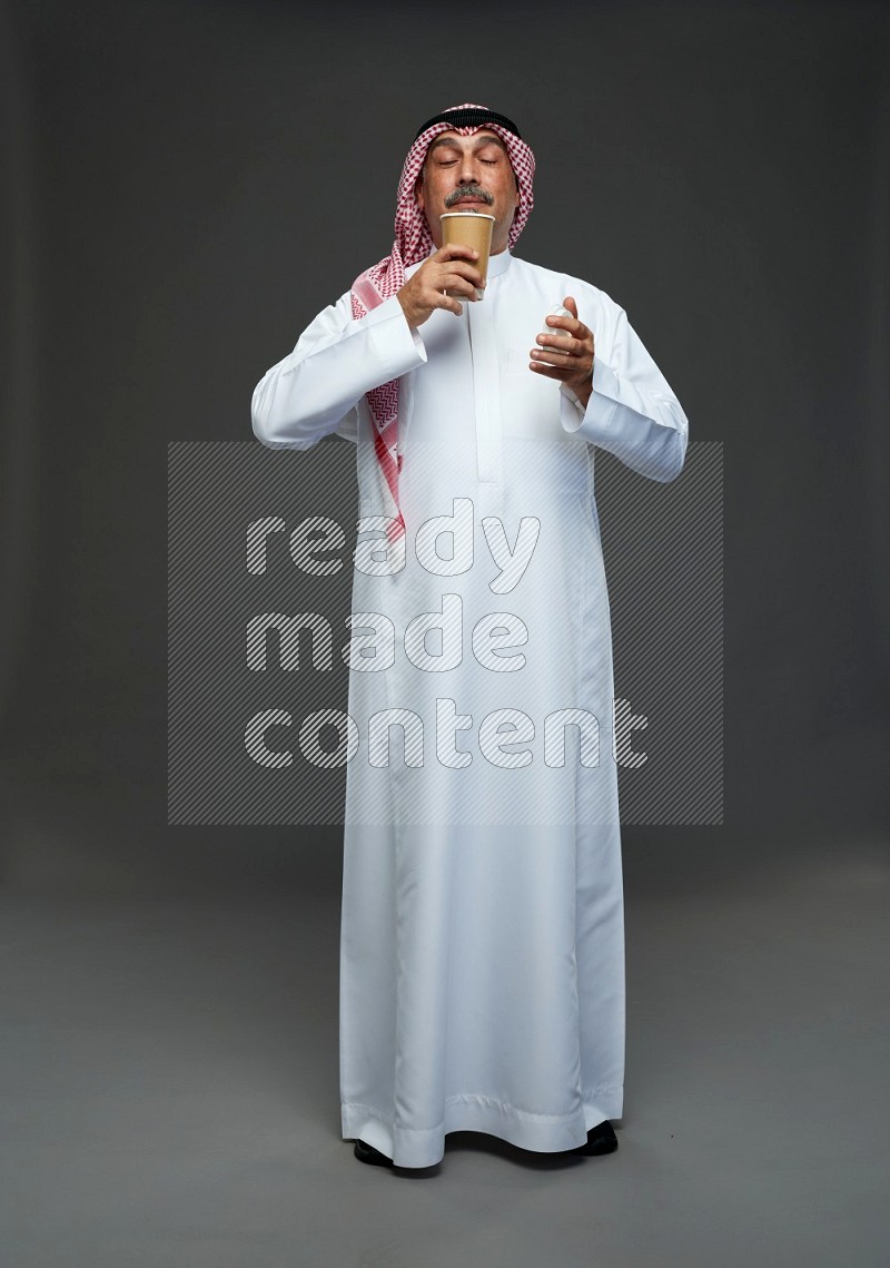 Saudi man with shomag Standing holding paper cup on gray background