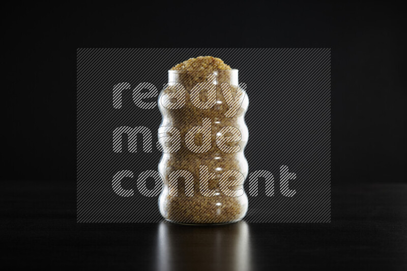 Coarse bulgur in a glass jar on black background