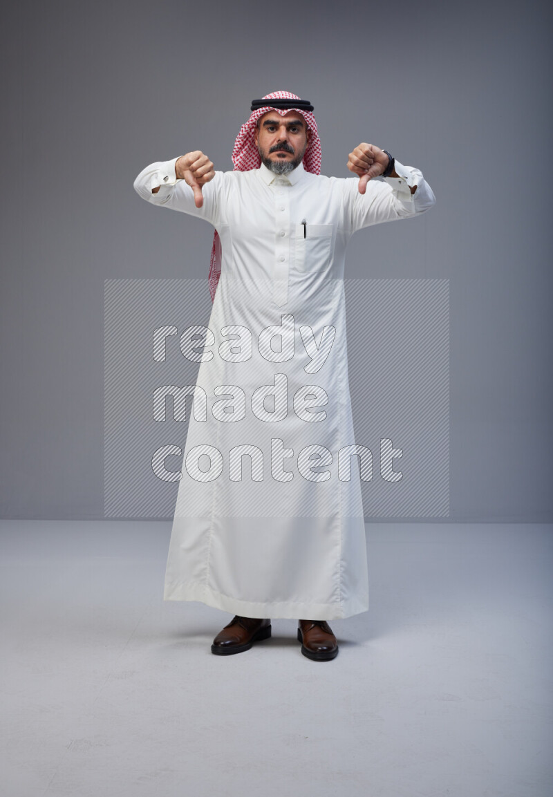 Saudi man Wearing Thob and red white Shomag standing interacting with the camera on Gray background