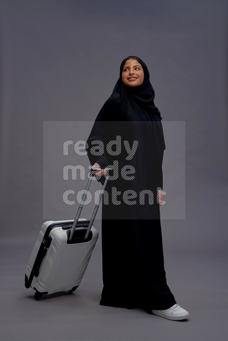 Saudi woman wearing Abaya standing holding bag on gray background