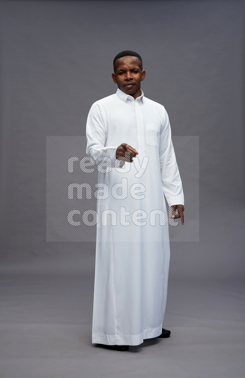 Saudi man wearing thob standing interacting with the camera on gray background