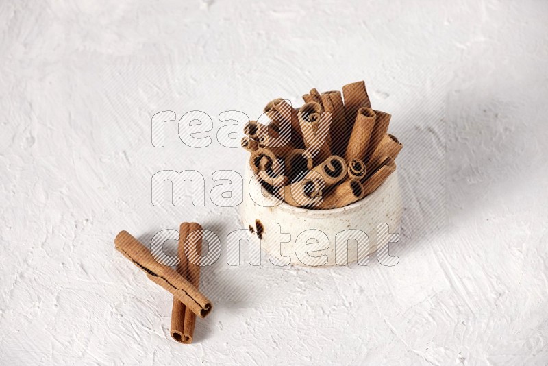 Cinnamon sticks in a beige bowl on a white background