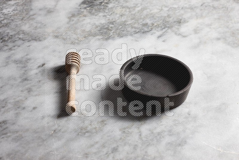 Black Pottery bowl with wooden honey handle on the side with grey marble flooring, 45 degree angle