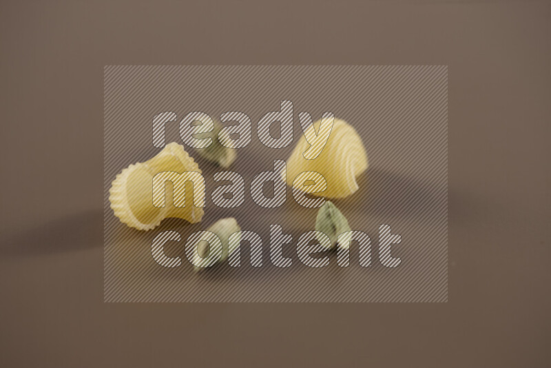 Raw pasta with different ingredients such as cherry tomatoes, garlic, onions, red chilis, black pepper, white pepper, bay laurel leaves, rosemary and cardamom on beige background