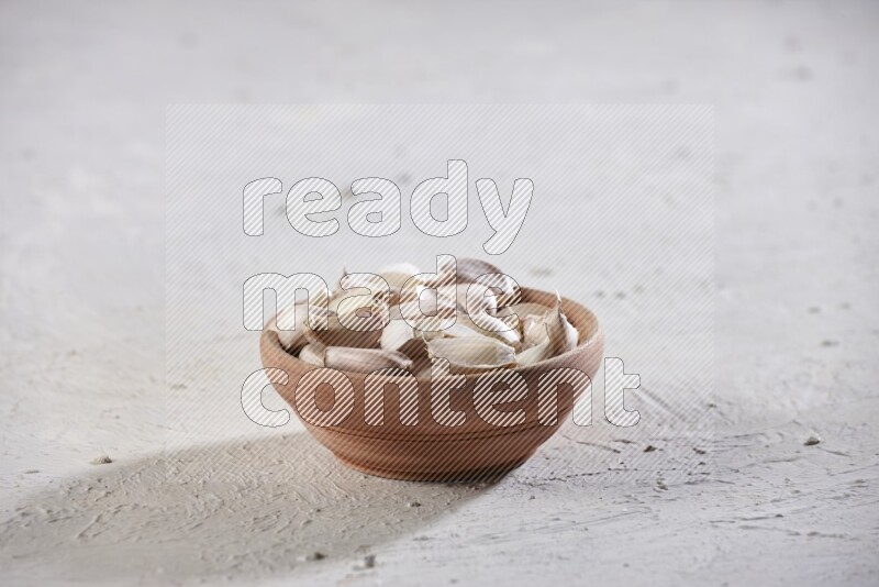 A wooden bowl full of garlic cloves on a white flooring
