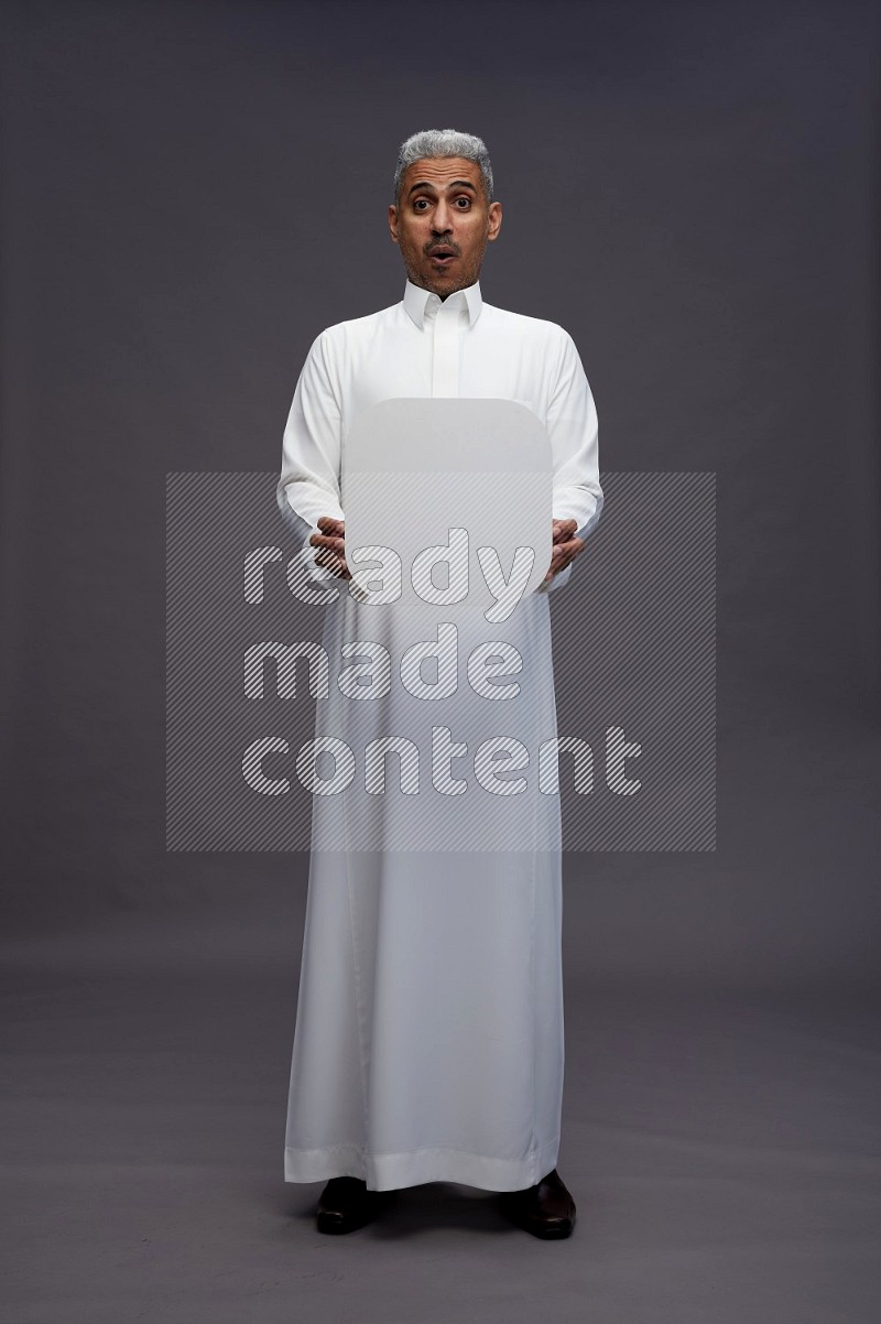 Saudi man wearing thob standing holding social media sign on gray background