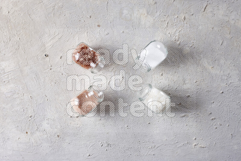 4 glass jars filled with table salt, coarse sea salt, fine himalayan salt and coarse himalayan salt on white background